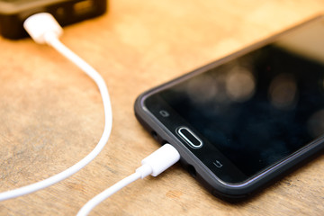 The phone is charging with powerbank on wood background