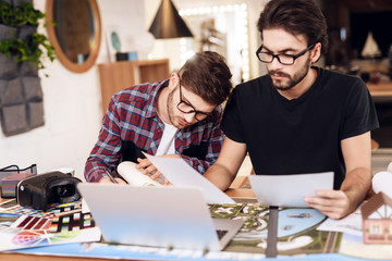 Two freelancer men taking notes at laptop at desk.