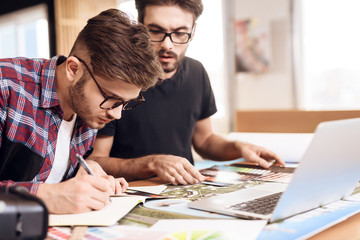 Two freelancer men taking notes at laptop at desk.