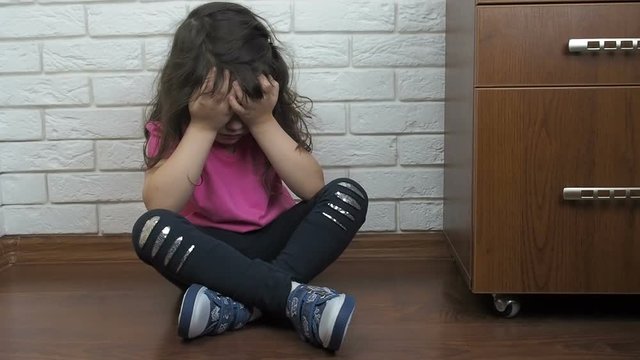 An unhappy child. A little girl is sitting on the floor and hiding her face.