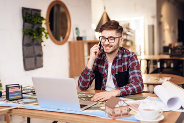 Freelancer man talking on the phone at laptop sitting at desk.