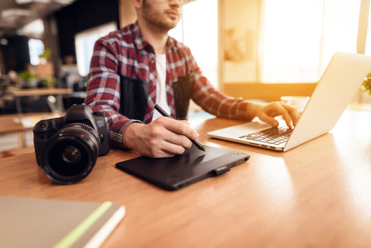 Freelancer man typing and drawing at laptop sitting at desk.