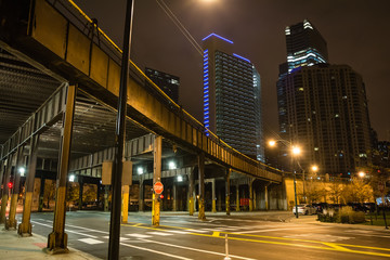 Urban city street corner with vintage train bridge and skyscrapers in Chicago at night