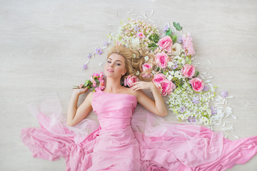 TOP VIEW: Portrait of a beautiful young girl in a pink dress lies on a floor with a flowers