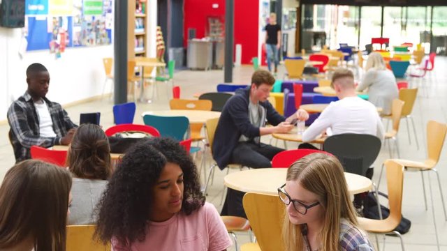 Female Students Working In Communal Area Of Busy College Campus 