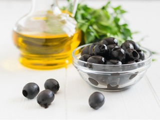 Olives and a bottle of olive oil on a white wooden table.