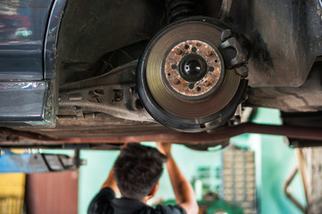 Auto mechanic asian checking bush-bolt under double wishbone suspension by hand with tools car lift 