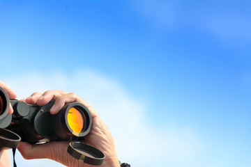 hand holding binoculars on blue sky background