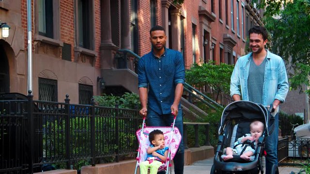 Two father friends walking in the street pushing strollers