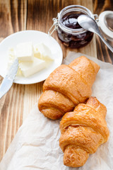 two croissants, butter and jam on a wooden table. © Lazy_Bear