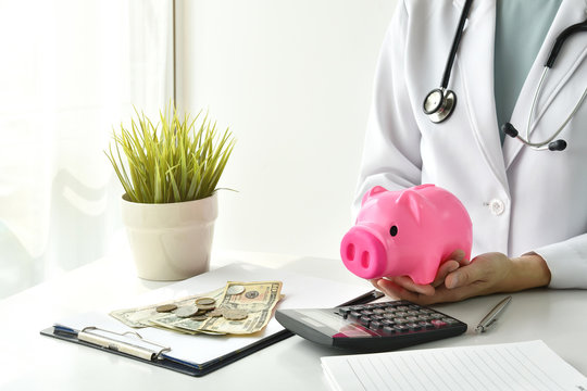 Medical And Health Insurance Concept, Doctor Holding Piggy Bank And Money In Hospital Background, Money Saving For Medical Care Expenses.