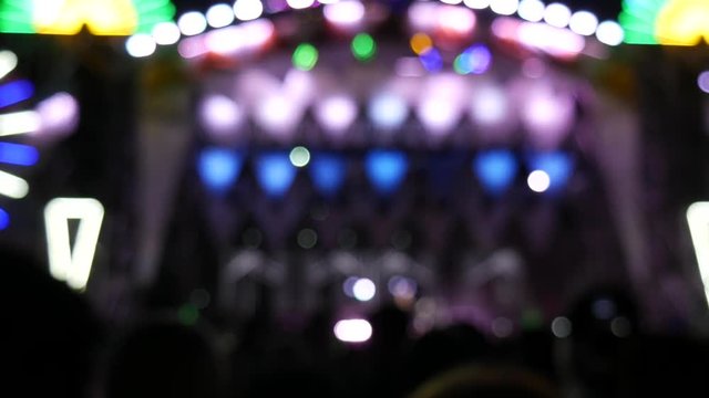 Blurred background of colored lights from the stage at a live music festival at night. Blur people dancing to the rhythm of the music. Light and color with beautiful in the concert at night.
