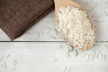 A wooden spoon filled with rice placed on wooden background.