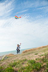 happy funny little boy with kite in his hands jumped high against background of sea coast