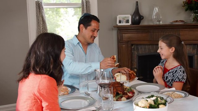 Jewish man sharing challah bread with family at Shabbat meal