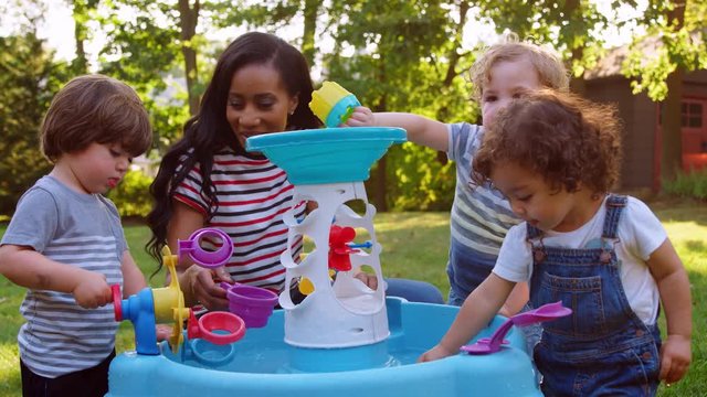 Mother And Young Children Playing With Water Table In Garden