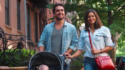 Happy couple walking in the street with baby in a stroller