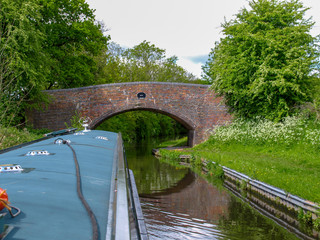 A narrowboat approaches a bridge on the Staffordshire and Worcestershire Canal in Staffordshire, England. View from the helmsman on the boat.