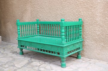 The old wooden sofa is green. An ancient oriental wooden sofa is located on the street.