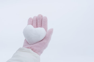 Hands in pink gloves holding snow heart
