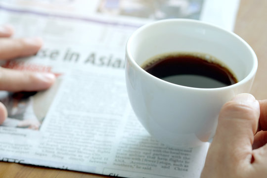 Man holding a cup of coffee in the background reading a newspaper.