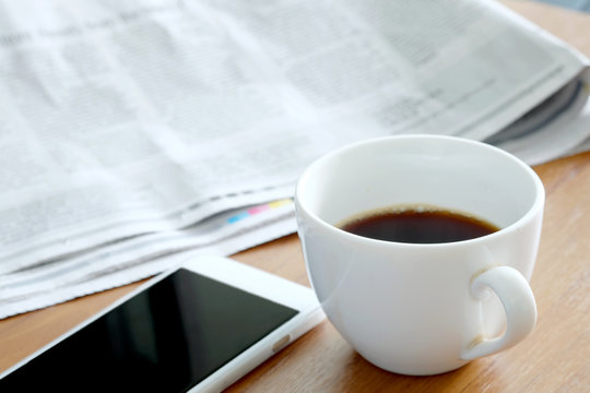Coffee cup and smartphone on desk, newspaper background