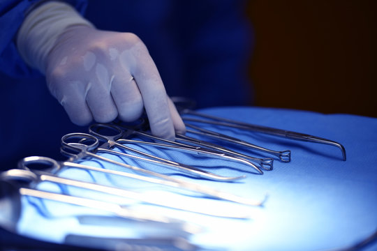 Surgeon hand picking up an instrument from tray of surgical instruments