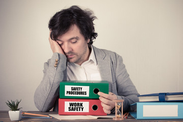 Work Safety and Safety Procedures text on the binders, worried bussinesman thinking by the work desk