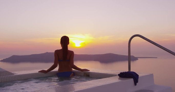 Resort Vacation - Woman In Swimming Pool Spa Enjoying Sunset Over Sea On luxury travel holidays on Santorini, Greece, Europe. RED EPIC SLOW MOTION
