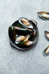 Overhead view of raw kiwi mussels in copper plate on textured light colored background with text space left