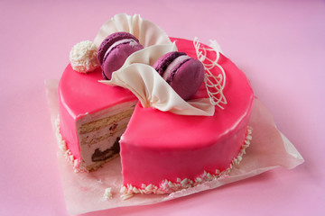 A beautiful cake in pink glaze decorated with macaroons. Decor of white chocolate. Pink background