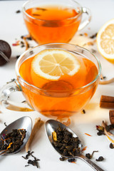 Two transparent cups of tea with a slice of lemon on a white background. Spoons, a filter for brewing, chopped lemon, cinnamon sticks. Concept. Different types of teas. Close up