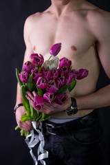 A young guy with a beautiful, naked torso holds in his hands a large bouquet of purple tulips