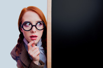 young redhead teacher with round glasses hiding behind a blackboard