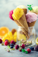 Colorful ice cream cones. Red, pink, yellow, green, white ice-cream balls with different flavors - mango, lime, mint, pistachio, orange, strawberries, raspberries, blueberries. Colorful summer concept