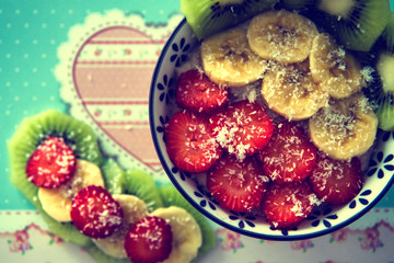 Oatmeal porridge with strawberries, kiwi, banana and coconut in a bowl on chopping board and fruits around.