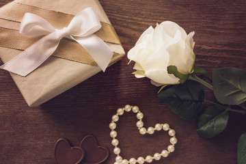 Beautiful rose, gift box with white ribbon and beads on brown wooden table. Lovely, romantic surprise for beloved. Woman's day and relationship concept. Decorative artificial flower.