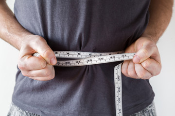 Slim man measuring his waist. Healthy lifestyle, body slimming, weight loss concept. Cares about...