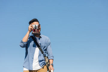 Happy Asian toursit taking vintage camera  with blue sky in sunny day.