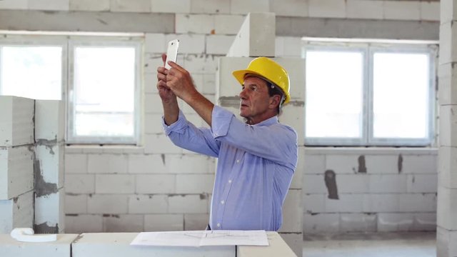 Senior architect with smartphone at the construction site.