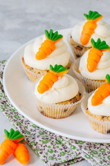 Vanilla cupcakes with chocolate chips and cream cheese frosting decorated with carrot marmalade in a plate on a white stone background.