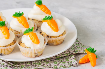 Vanilla cupcakes with chocolate chips and cream cheese frosting decorated with carrot marmalade in a plate on a white stone background.