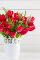 Fresh red tulip flowers bouquet on shelf in front of wooden wall.