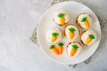 Vanilla cupcakes with chocolate chips and cream cheese frosting decorated with carrot marmalade in a plate on a white stone background.