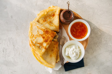 Delicious crepes (blinis) with assorted sauces on a wooden board on a blue stone background.