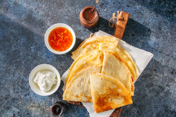 Delicious crepes (blinis) with assorted sauces on a wooden board on a blue stone background.