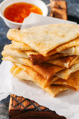 Delicious crepes (blinis) with assorted sauces on a wooden board on a blue stone background.