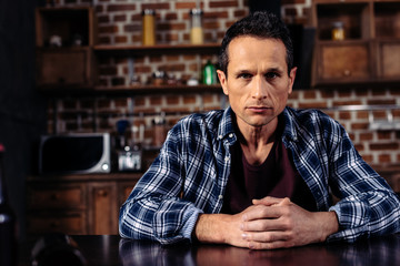 portrait of lonely man sitting at table in kitchen at home