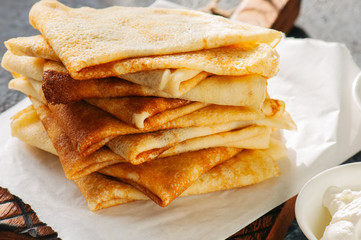 Delicious crepes (blinis) with assorted sauces on a wooden board on a blue stone background.