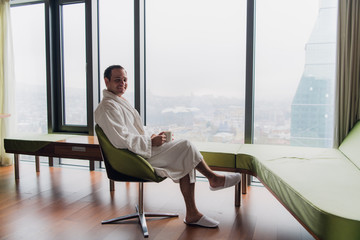 Man in bathrobe drinking coffee, looking at cityscape